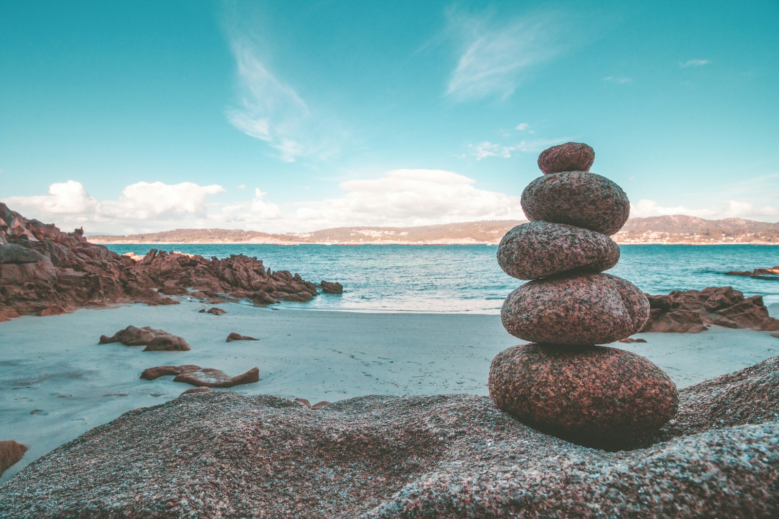A balanced stack of smooth stones on a beach beneath a blue sky